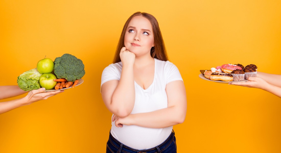 Photo of a young woman choosing between cake or vegetables